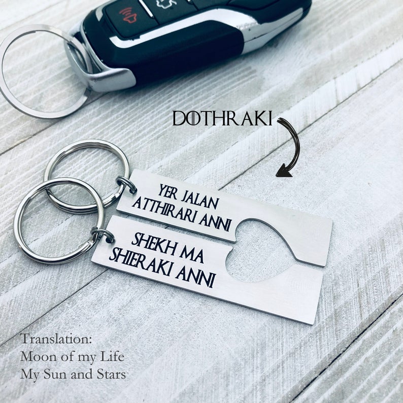 Two silver stainless steel keychains with Dothraki engraving, presented on a car key. One keychain reads 'Yer Jalan Atthirari Anni' and the other reads 'Shekh Ma Shieraki Anni', with optional personalization. Game of Thrones Gift