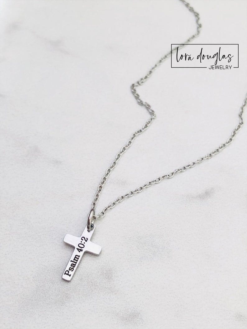 A silver stainless steel engraved cross necklace with a lobster clasp and a small cross charm, placed on a white surface