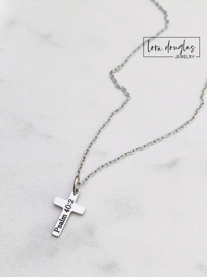 A silver stainless steel engraved cross necklace with a lobster clasp and a small cross charm, placed on a white surface