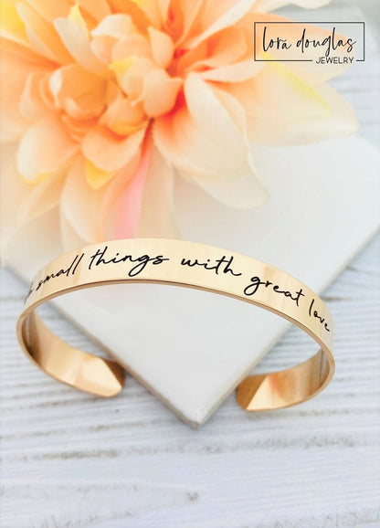 gold stainless steel cuff bracelet with an engraved message 'Do small things with great love'.