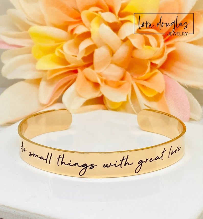 gold stainless steel cuff bracelet with an engraved message 'Do small things with great love'.