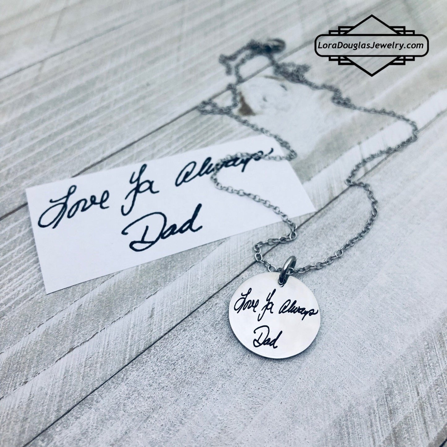 A round silver pendant with engraved with handwritten text 