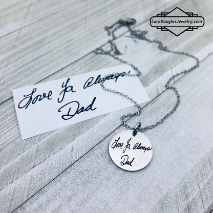 A round silver pendant with engraved with handwritten text 