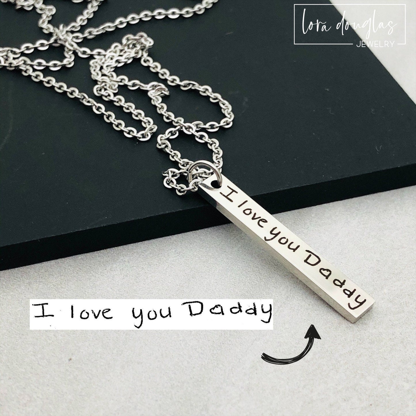 A silver stainless steel pendant necklace engraved with a handwritten message on a chain.