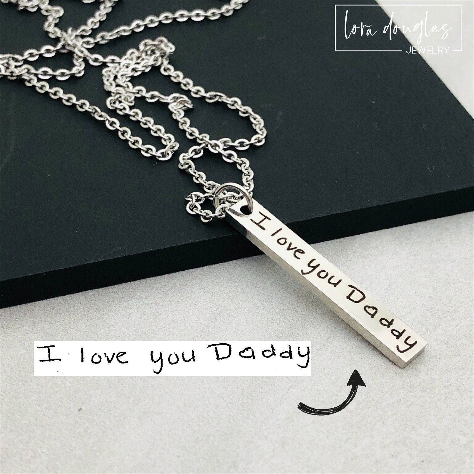A silver stainless steel pendant necklace engraved with a handwritten message on a chain.