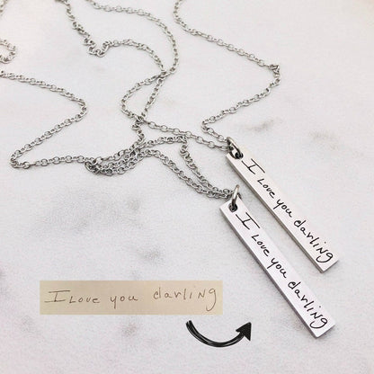 A silver stainless steel pendant necklace engraved with a handwritten message on a chain.