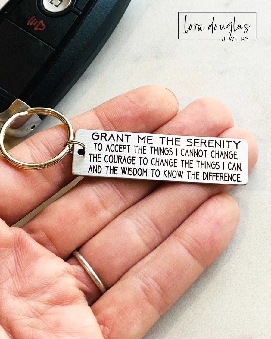 A stainless steel keychain with the serenity prayer engraved on it, attached to a car key.