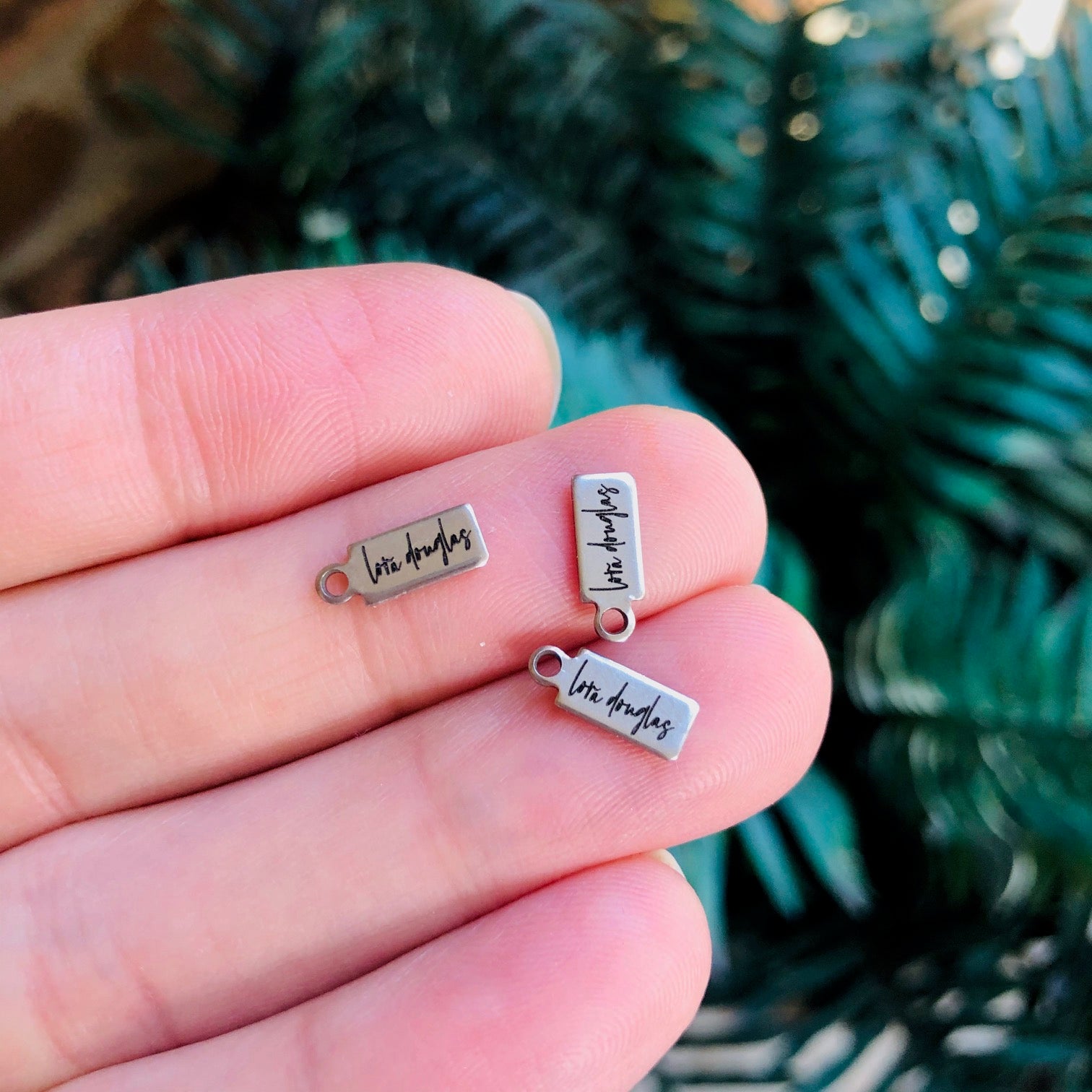 A collection of stainless steel jewelry tags with laser engraved logos and text on a white surface.