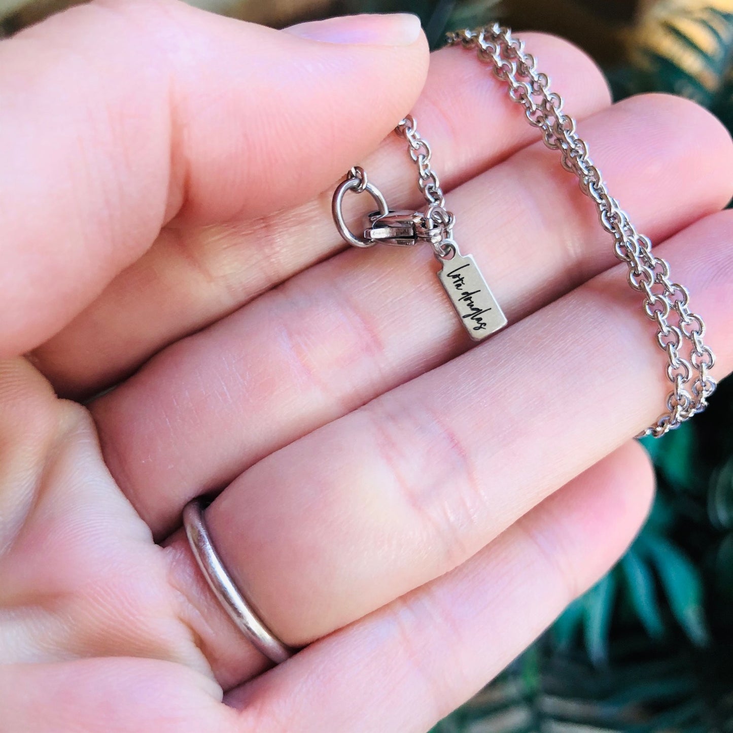 A collection of stainless steel jewelry tags with laser engraved logos and text on a white surface.