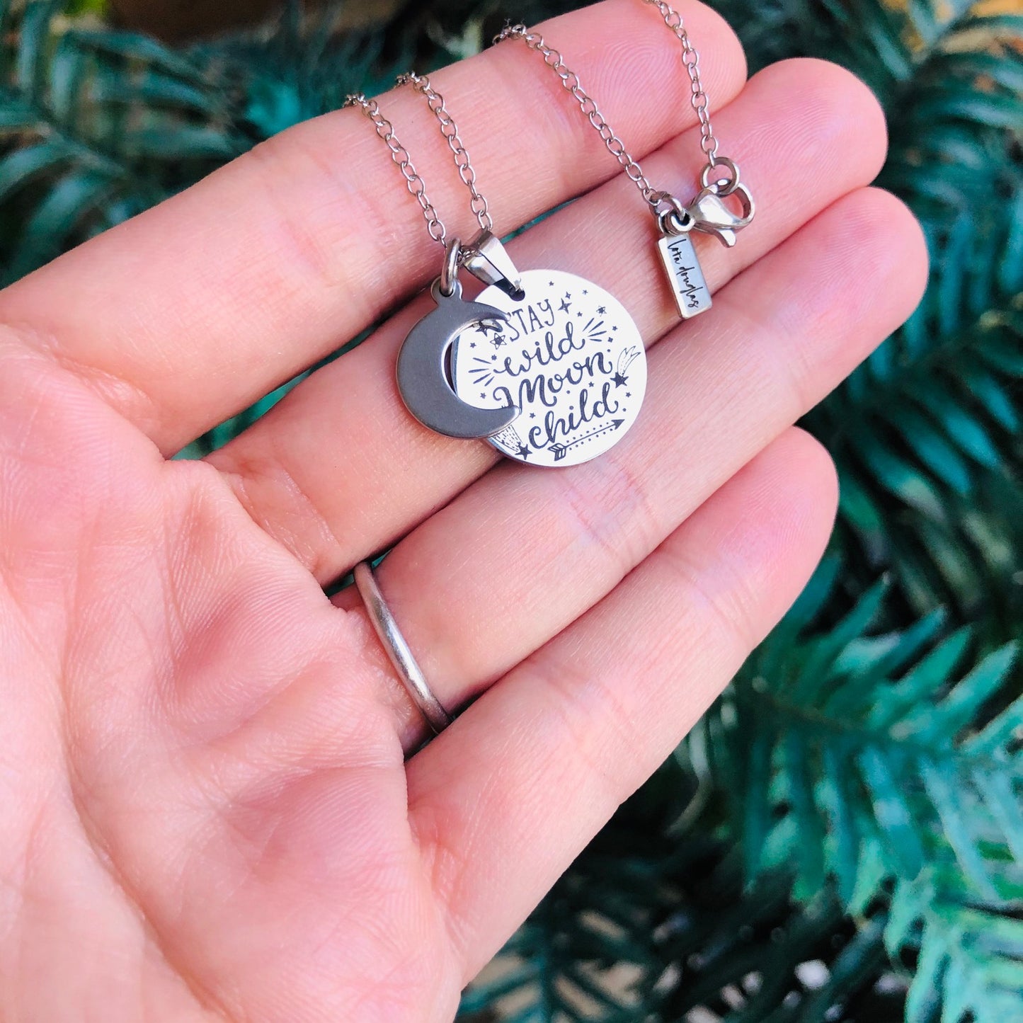 A collection of stainless steel jewelry tags with laser engraved logos and text on a white surface.