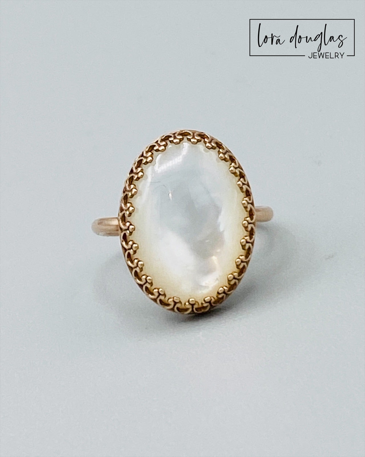 A bronze ring with a mother of pearl stone set in a gold-colored setting.
