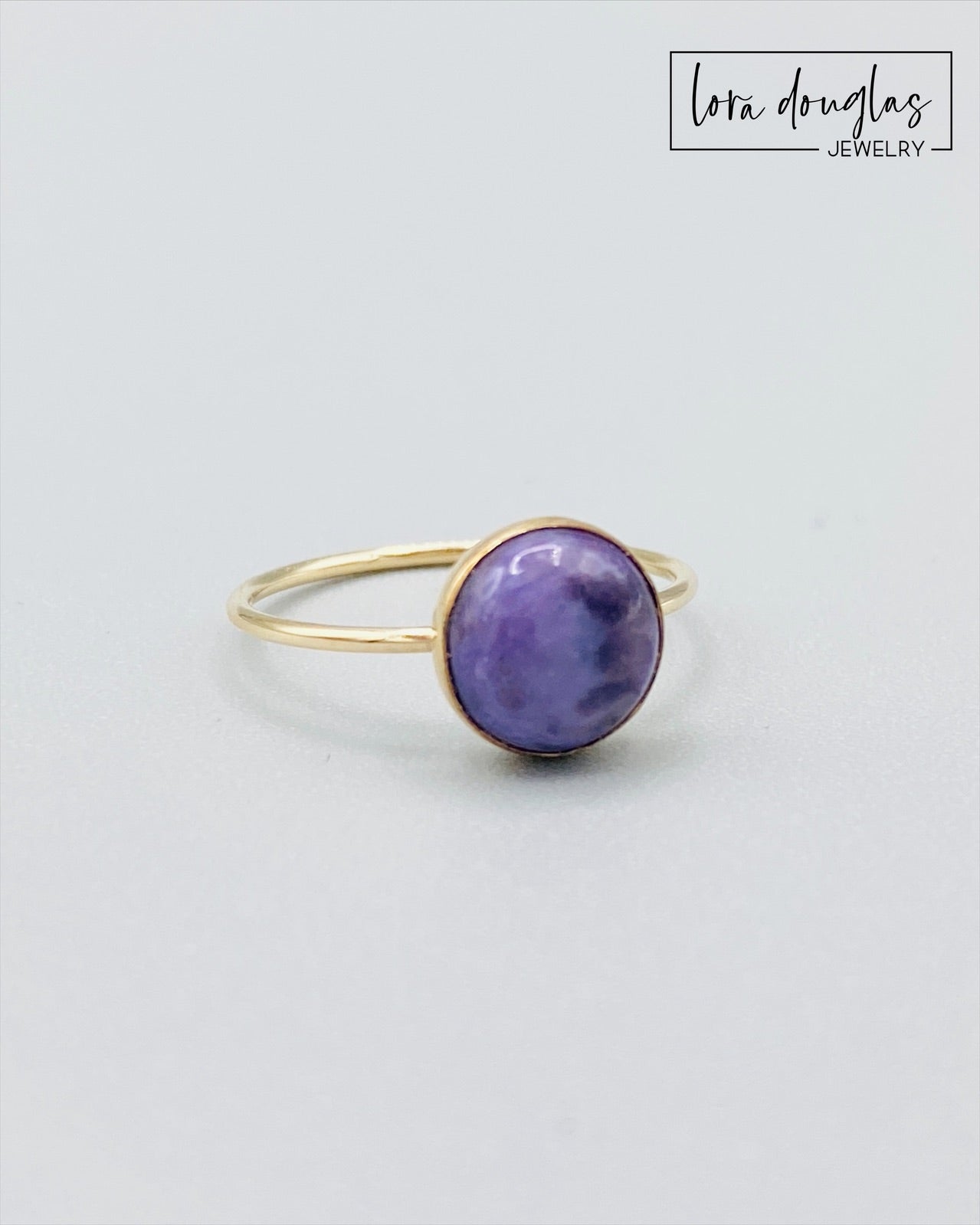 Gold-filled ring with a purple charoite stone set in a gold-filled band, displayed against a white background.