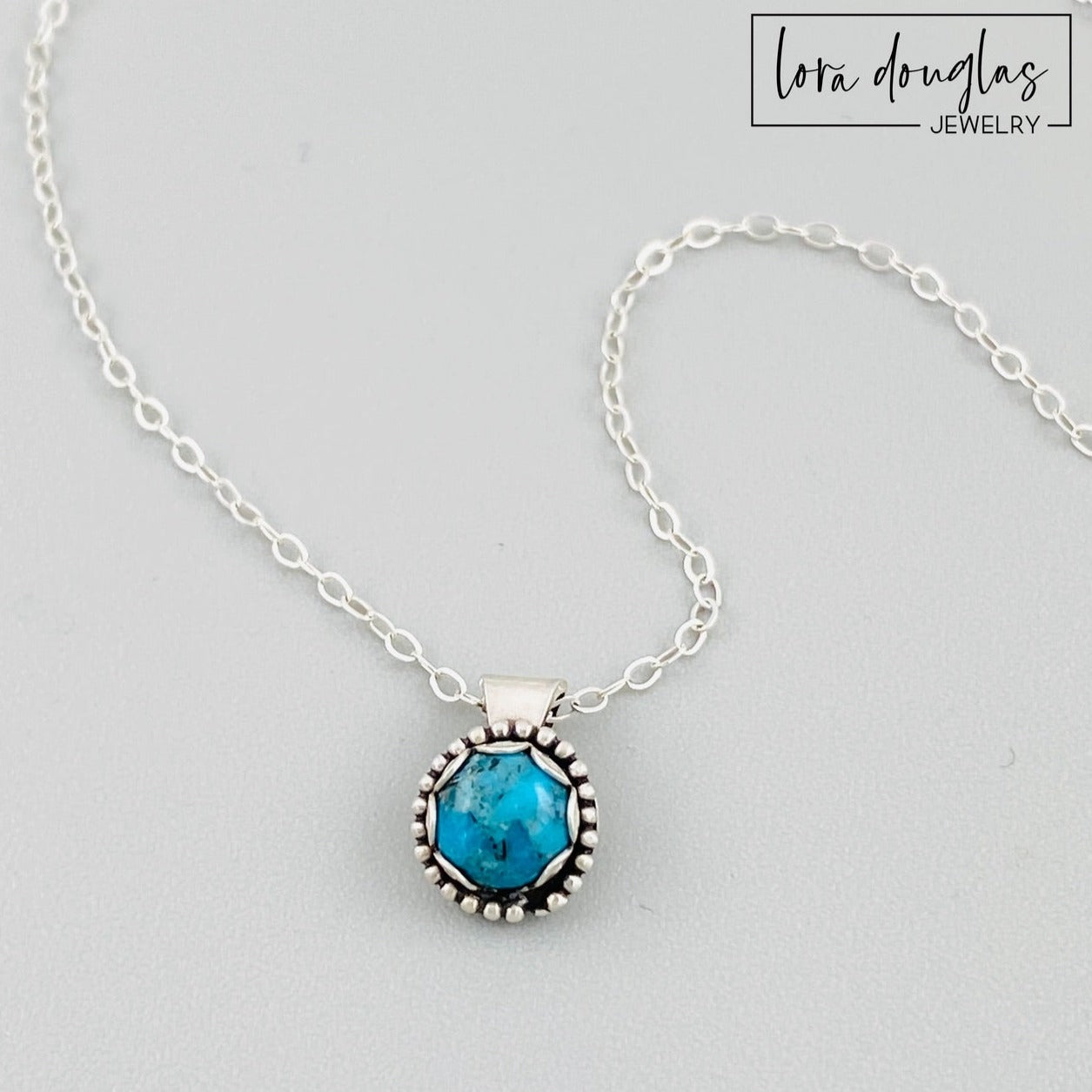 A sterling silver pendant necklace with a turquoise stone and a silver chain with an antique patina finish.