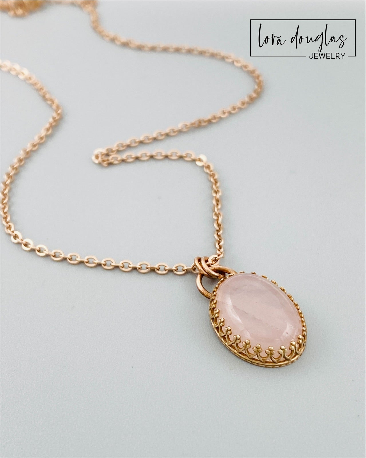 A bronze necklace with a rose quartz pendant, featuring a lobster clasp.