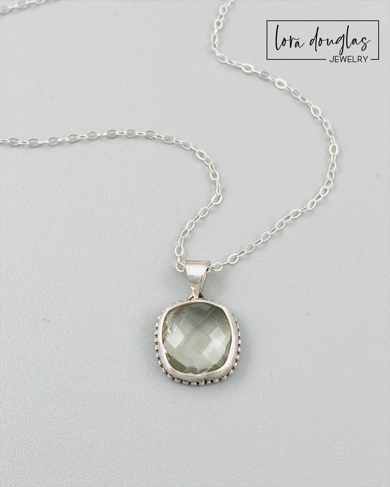 A sterling silver pendant necklace with a faceted green amethyst gemstone, attached to a silver chain.