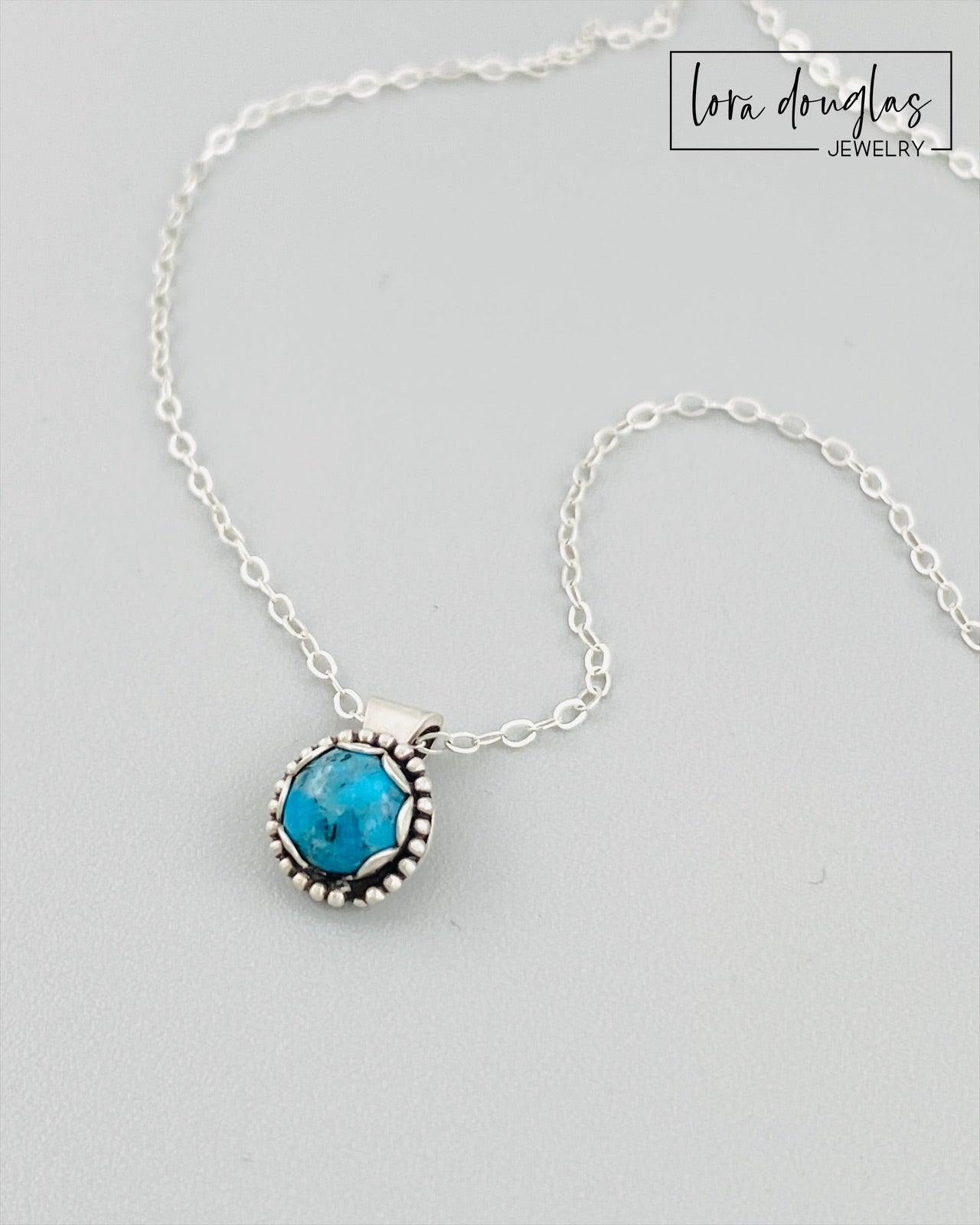 A sterling silver pendant necklace with a turquoise stone and a silver chain with an antique patina finish.