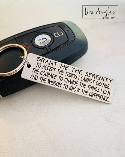 A stainless steel keychain with the serenity prayer engraved on it, attached to a car key.