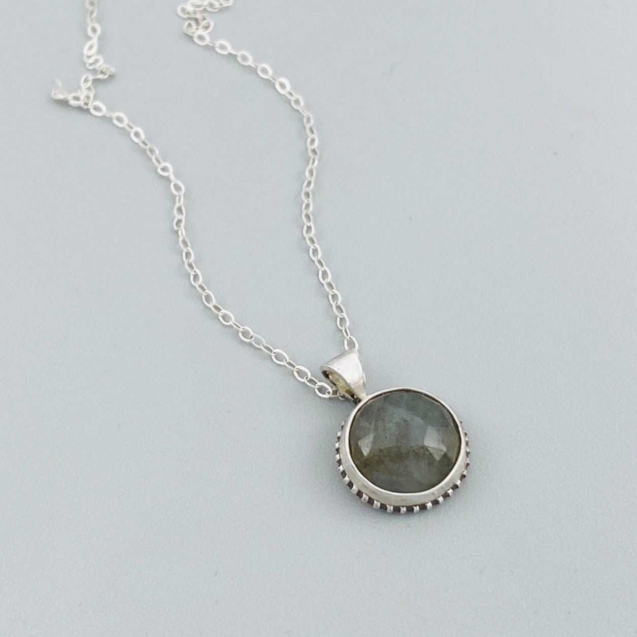 A sterling silver pendant necklace with a faceted labradorite gemstone in the center, attached to an 18-inch chain with a C clasp.