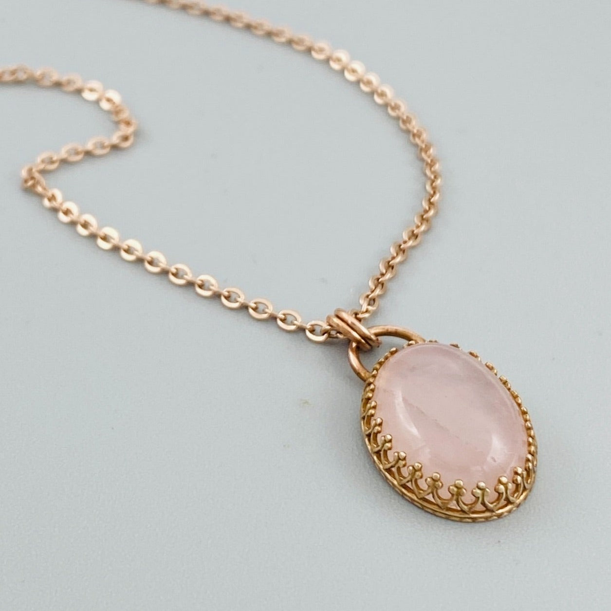 A bronze necklace with a rose quartz pendant, featuring a lobster clasp.