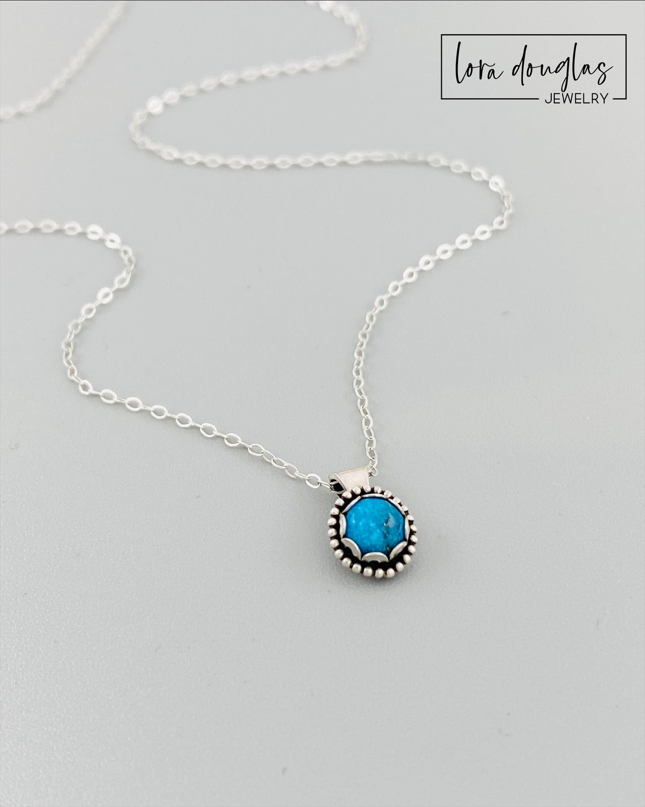 A sterling silver pendant necklace with a turquoise stone, displayed on a silver chain.
