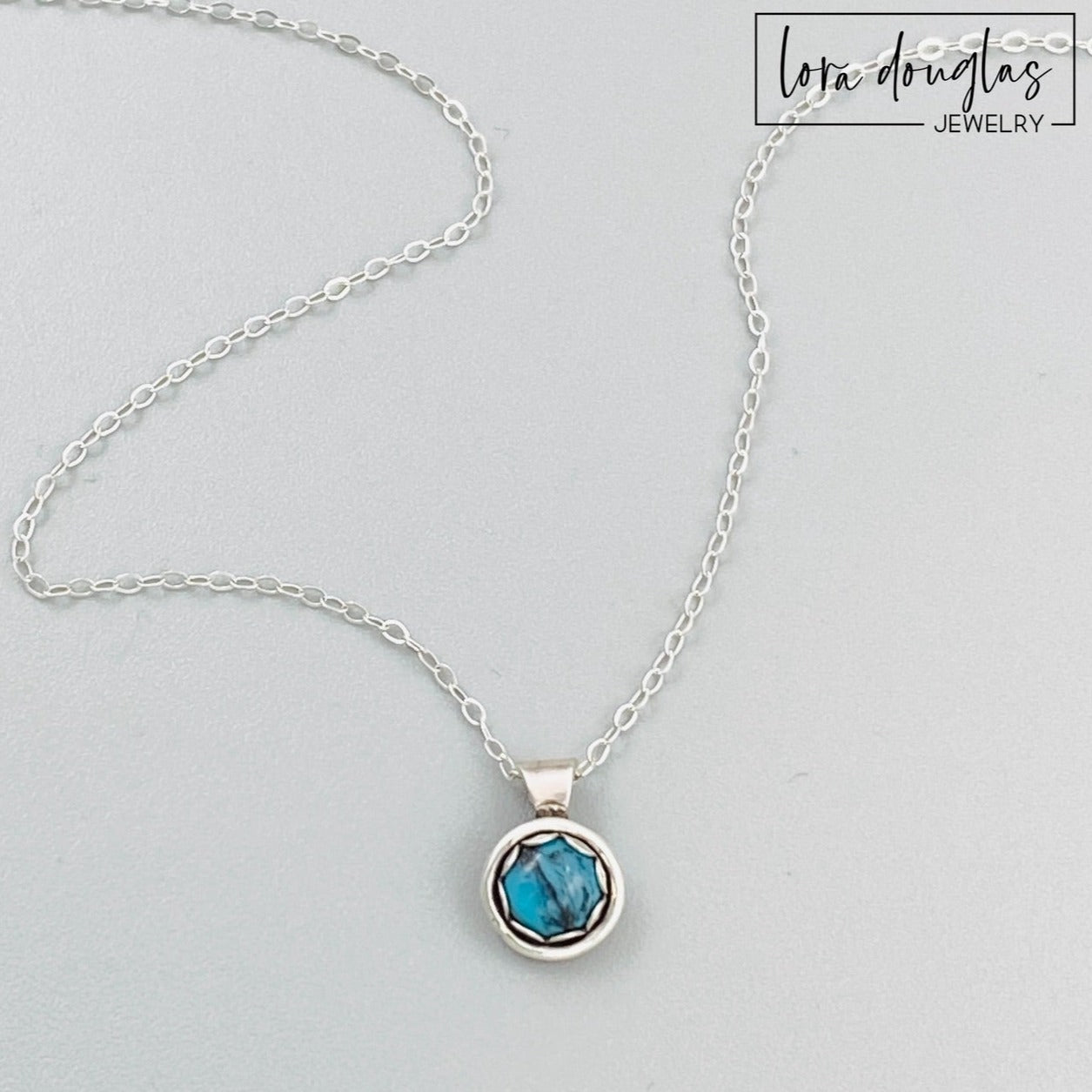 A sterling silver pendant necklace with a turquoise stone, displayed on a silver chain.