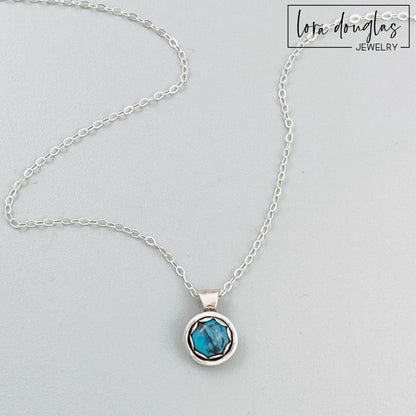 A sterling silver pendant necklace with a turquoise stone, displayed on a silver chain.