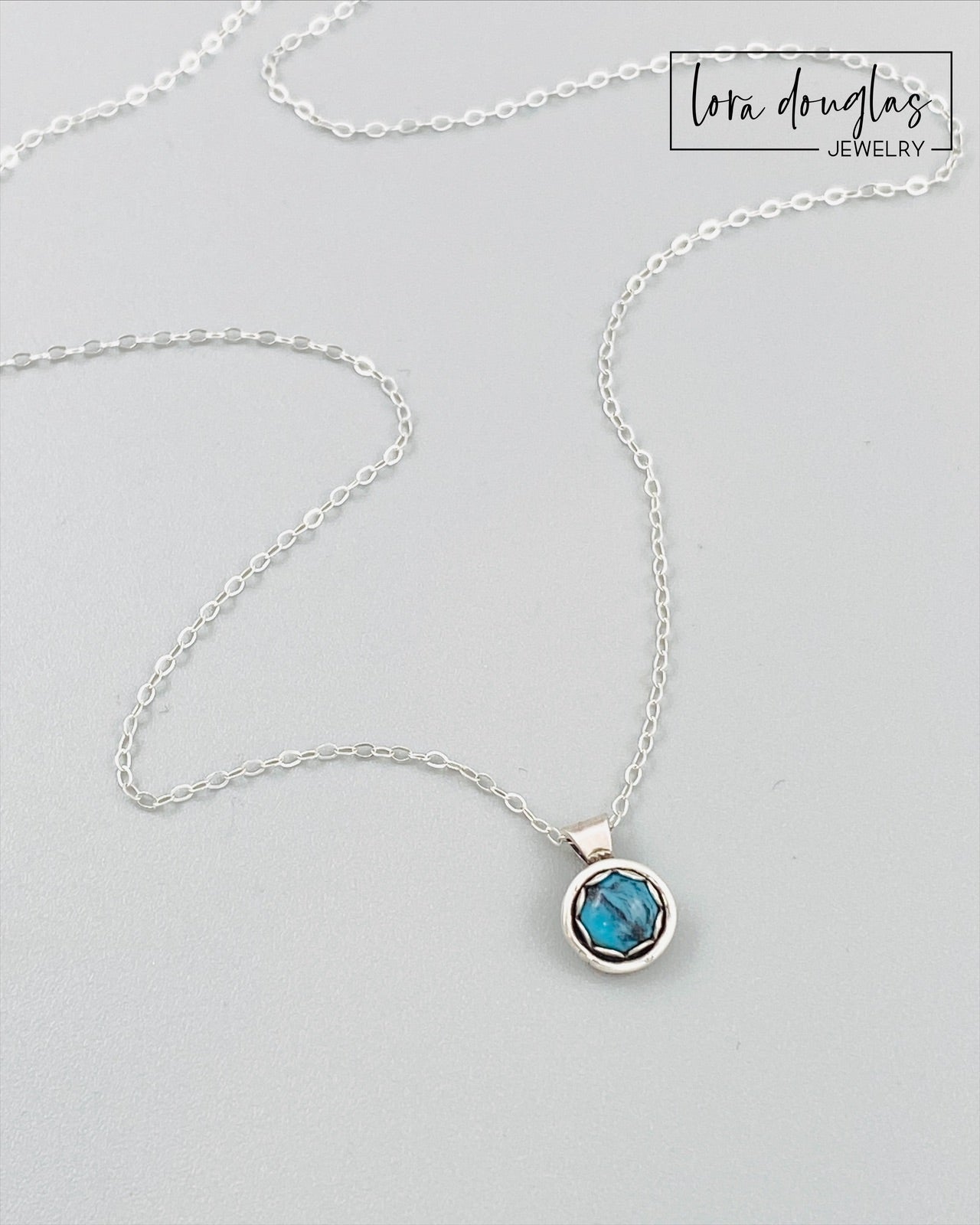 A sterling silver pendant necklace with a turquoise stone, displayed on a silver chain.
