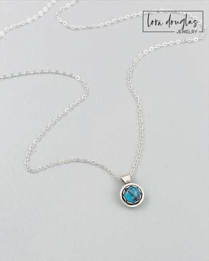 A sterling silver pendant necklace with a turquoise stone, displayed on a silver chain.