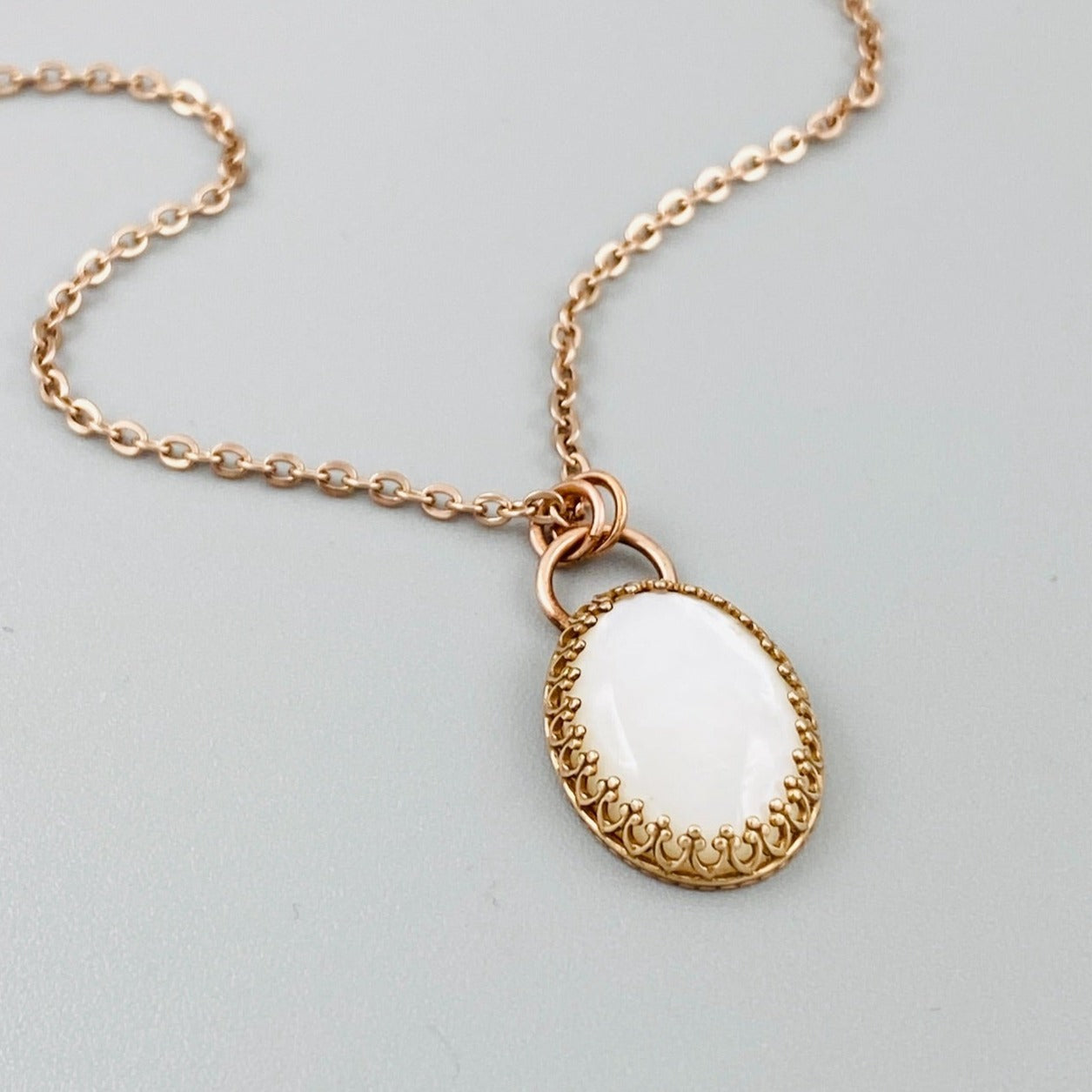 A bronze necklace with a stainless steel chain featuring a round moonstone pendant in a bronze setting.