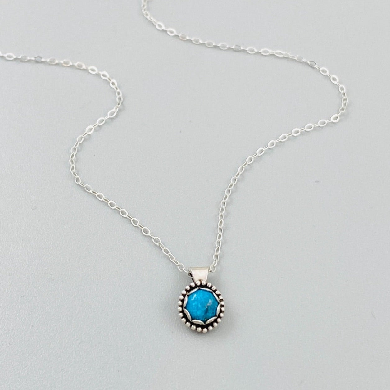 A sterling silver pendant necklace with a turquoise stone, displayed on a silver chain.