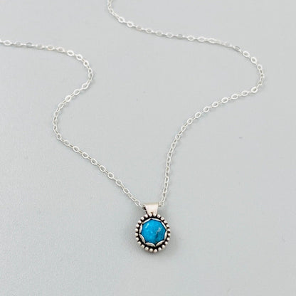 A sterling silver pendant necklace with a turquoise stone, displayed on a silver chain.