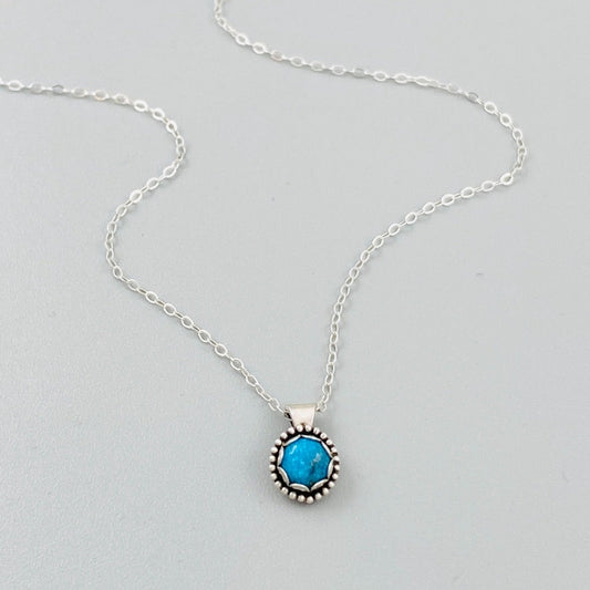 A sterling silver pendant necklace with a turquoise stone, displayed on a silver chain.