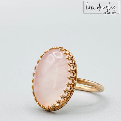A rose quartz ring with a bronze band, displayed against a white background.