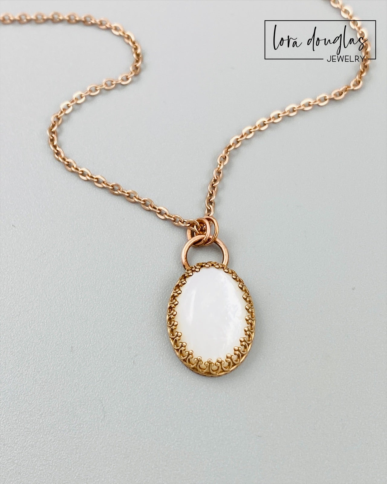 A bronze necklace with a stainless steel chain featuring a round moonstone pendant in a bronze setting.