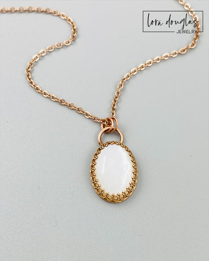 A bronze necklace with a stainless steel chain featuring a round moonstone pendant in a bronze setting.
