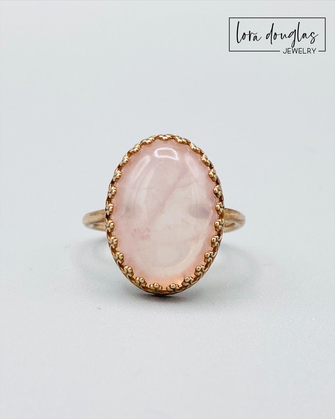 A rose quartz ring with a bronze band, displayed against a white background.