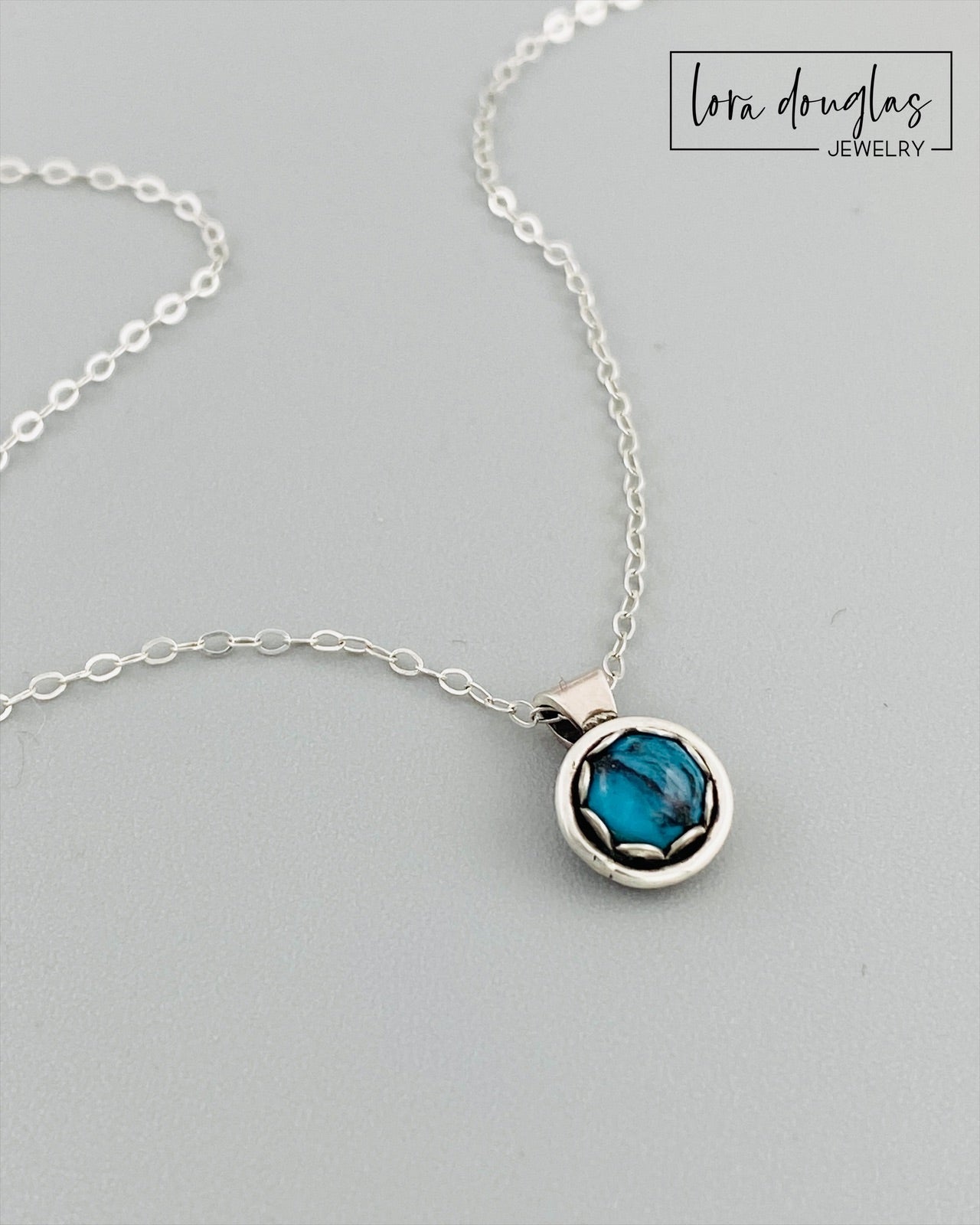 A sterling silver pendant necklace with a turquoise stone, displayed on a silver chain.