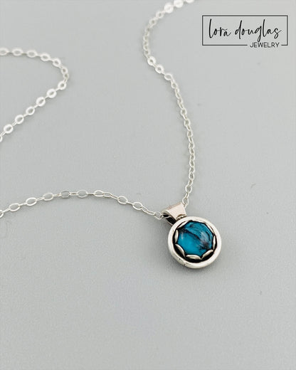 A sterling silver pendant necklace with a turquoise stone, displayed on a silver chain.