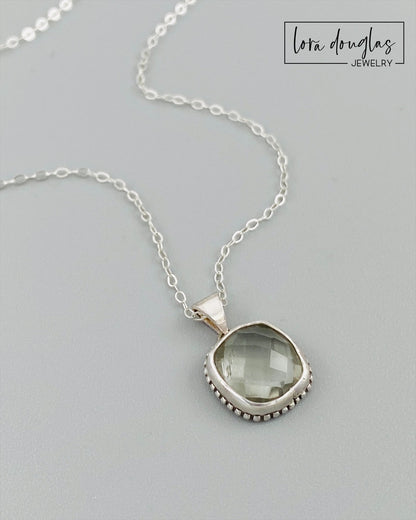 A sterling silver pendant necklace with a faceted green amethyst gemstone, attached to a silver chain.