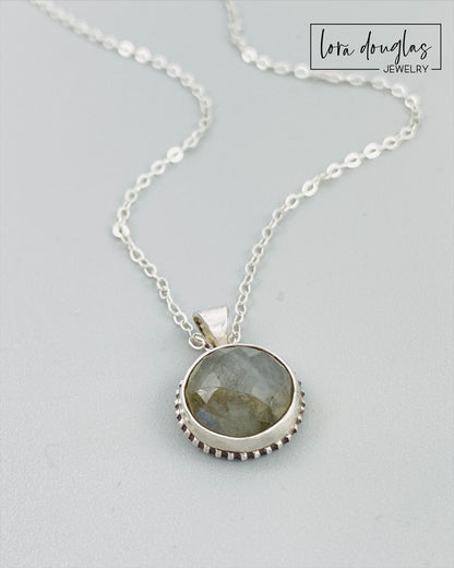 A sterling silver pendant necklace with a faceted labradorite gemstone in the center, attached to an 18-inch chain with a C clasp.