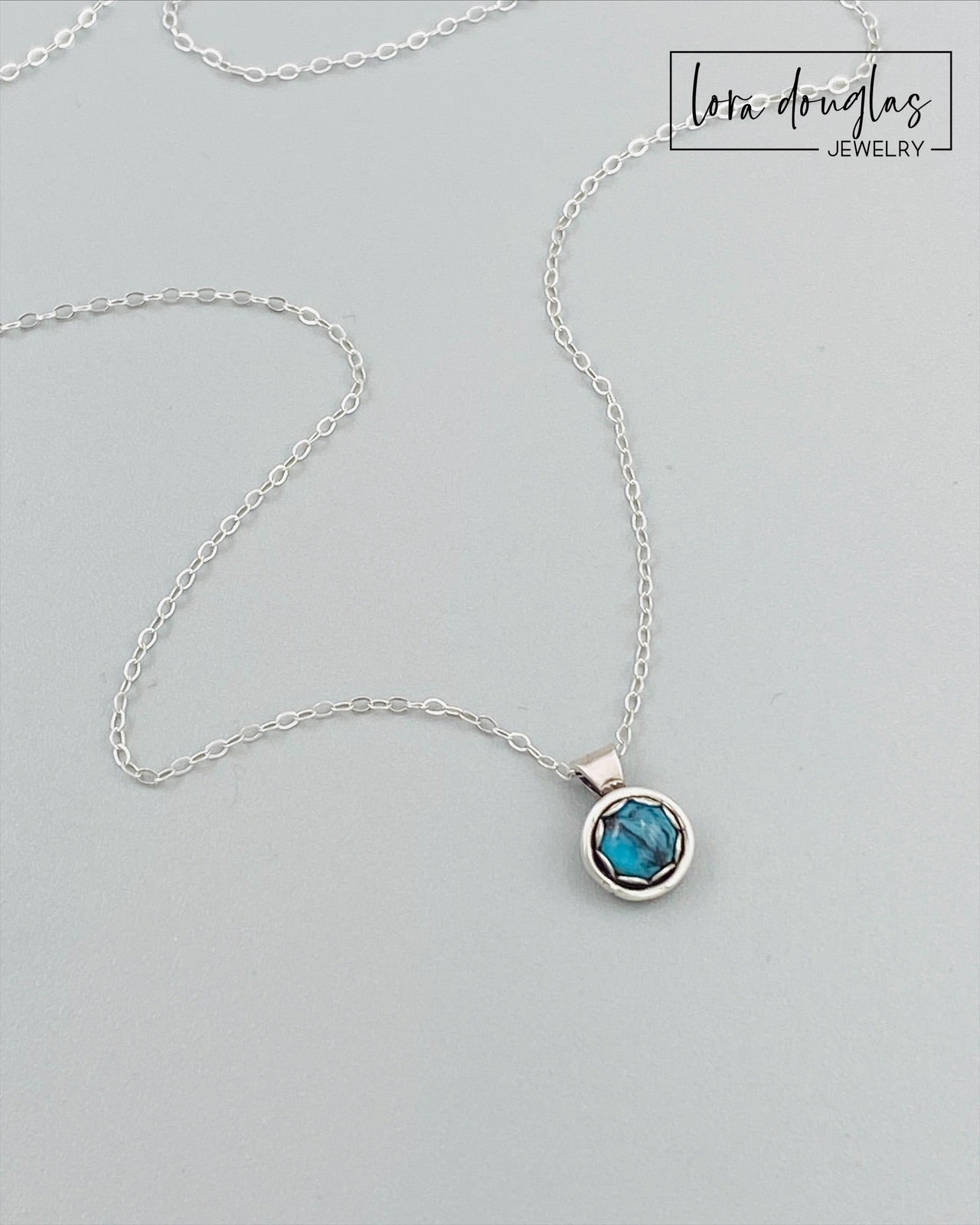 A sterling silver pendant necklace with a turquoise stone, displayed on a silver chain.