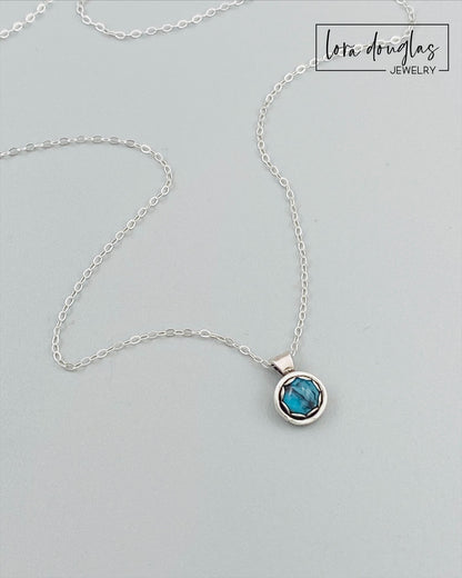 A sterling silver pendant necklace with a turquoise stone, displayed on a silver chain.