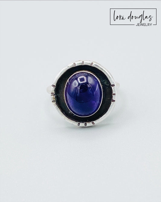 A sterling silver shadow box ring with a central amethyst stone, set in a circular silver setting.
