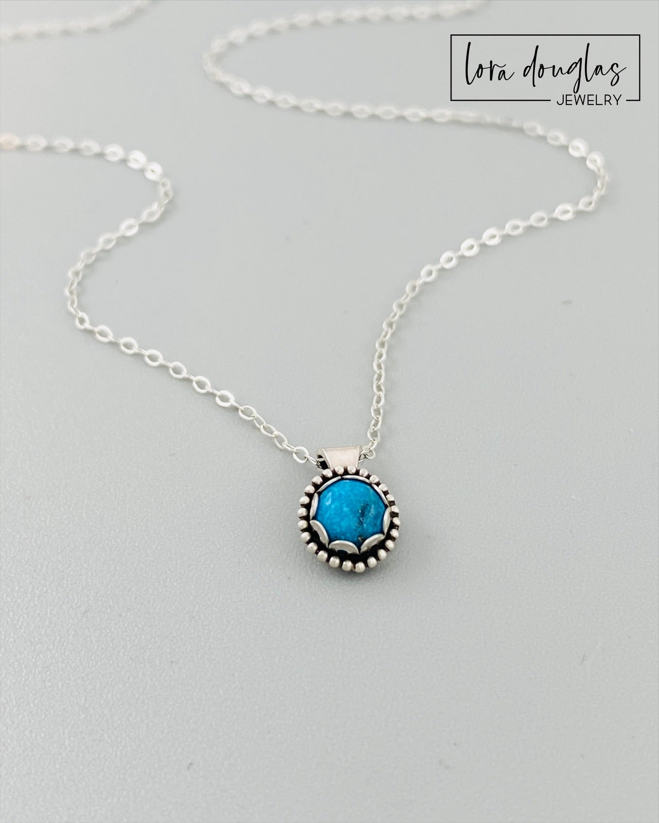 A sterling silver pendant necklace with a turquoise stone, displayed on a silver chain.
