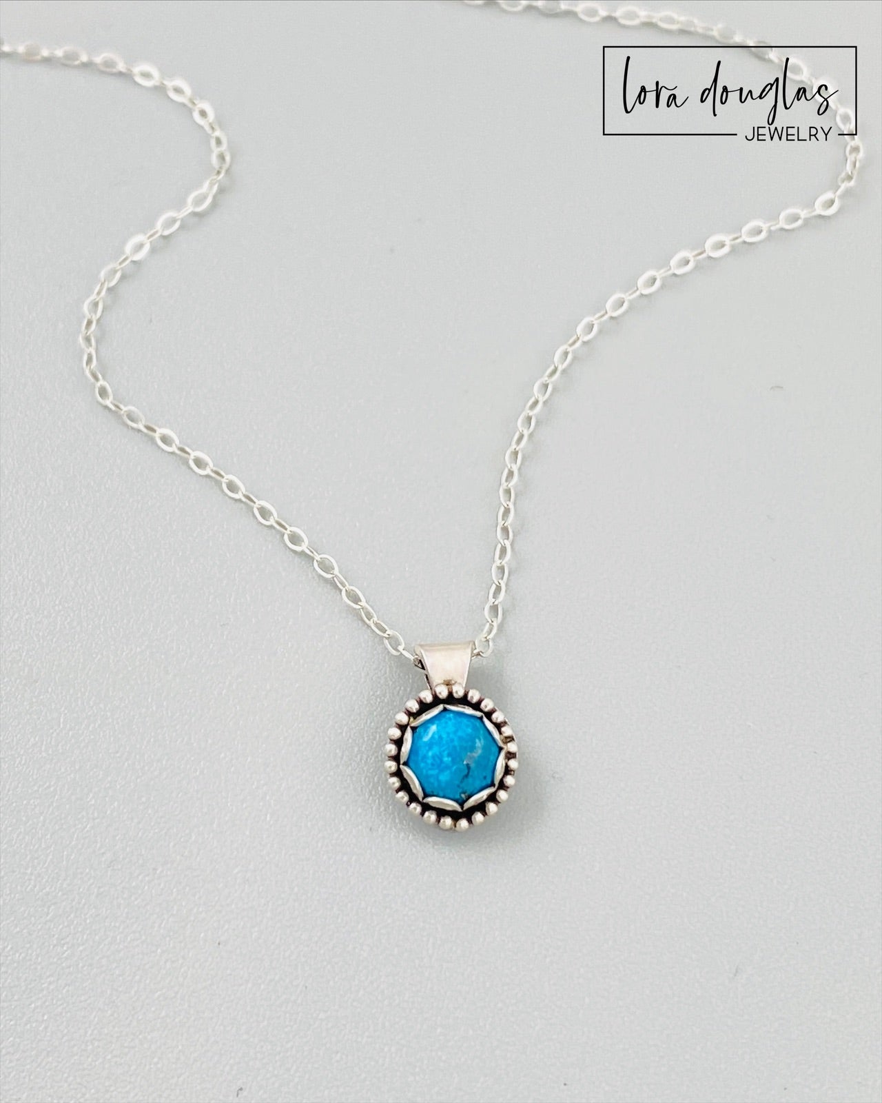 A sterling silver pendant necklace with a turquoise stone, displayed on a silver chain.