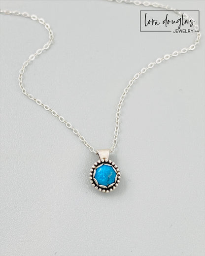 A sterling silver pendant necklace with a turquoise stone, displayed on a silver chain.