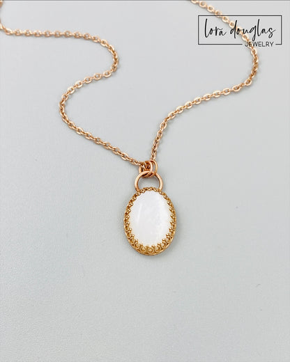 A bronze necklace with a stainless steel chain featuring a round moonstone pendant in a bronze setting.