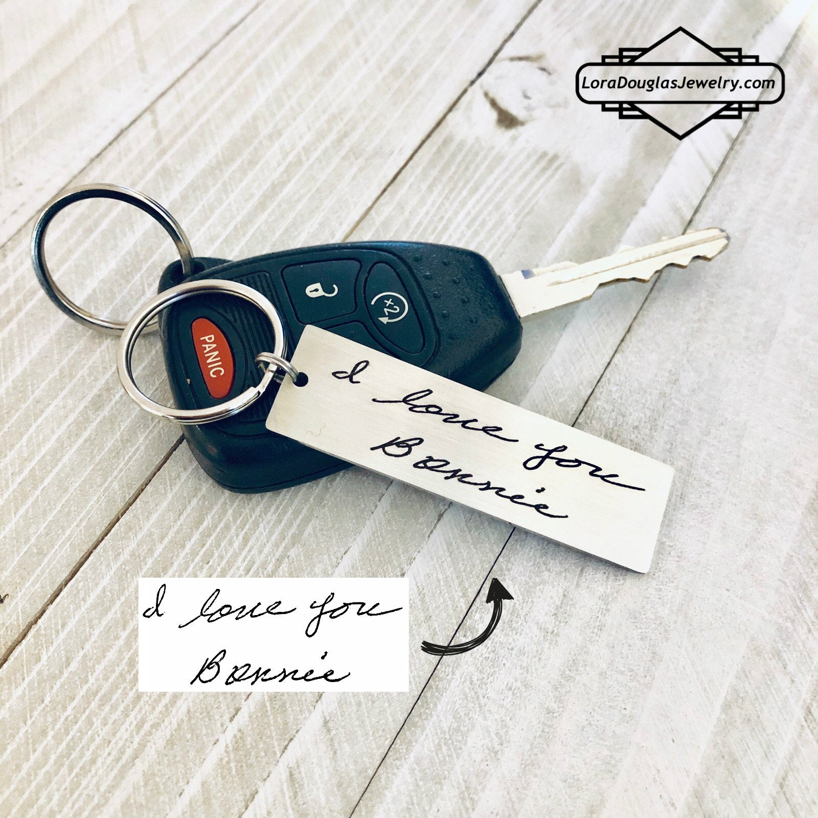 A stainless steel keychain with laser engraved handwriting on it, placed on a car key. 