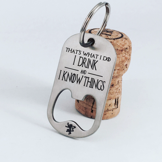 A stainless steel key chain with the engraved text 'That's What I Do I Drink and I Know Things' along with the HBO logo for Game of Thrones, resting on a corkscrew.