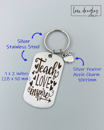 A silver stainless steel dog tag keychain with a silver pewter apple charm, engraved with the text 'Teach Love Inspire' accompanied by a heart symbol.